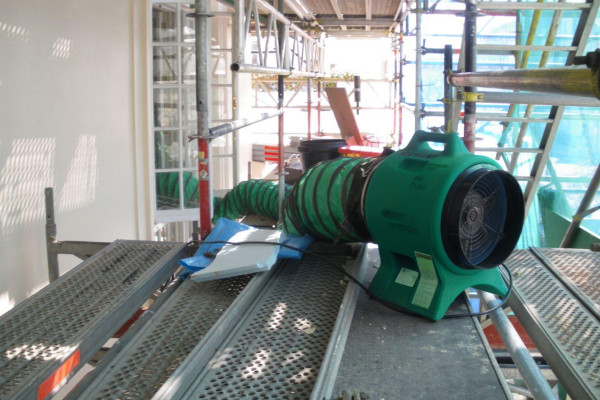 A VENTEX® Axial 300P Fan on top of metal scaffolding with ducting entering a nearby window