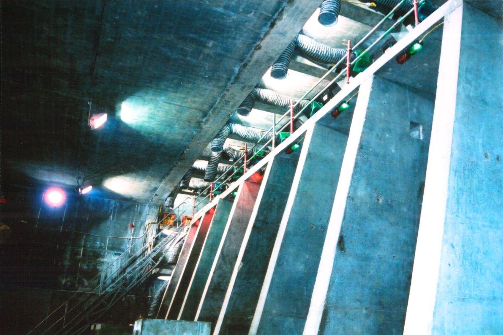 A row of VENTEX® Axial 300P Fans at the top of a large conrete wall with ducting hanging down at each pillar and a staircase at the far end