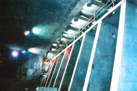 A row of VENTEX® Axial 300P Fans at the top of a large conrete wall with ducting hanging down at each pillar and a staircase at the far end