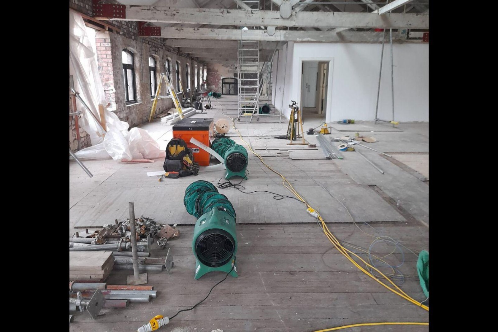 Two VENTEX® Axial 300P Fans one in front of the other on boarded floor, in a room with bare brickwork whilst renovation work takes place